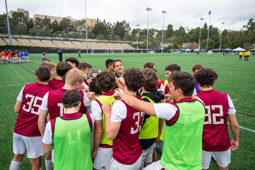 A group of guys in soccer jerseys huddle together to conduct a chant.