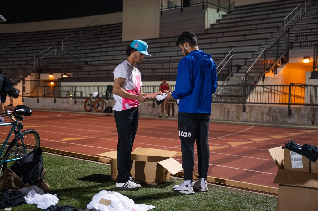 A man gives a sealed jersey to another man on a track.