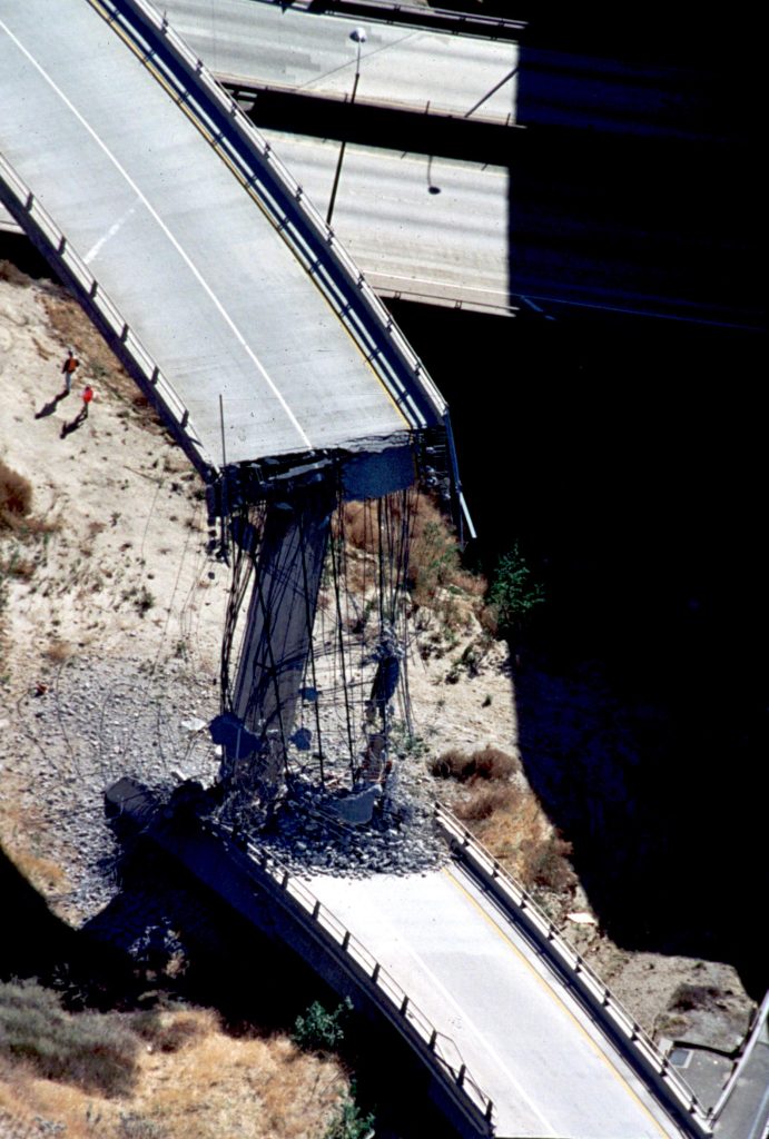 Aerial view of collapsed freeway bridge with exposed and damaged steel rebar.