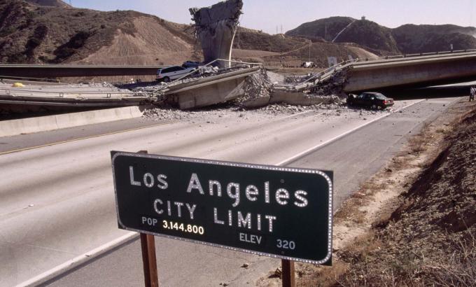 Sign reading "Los Angeles City Limit" on the side of the freeway is in the foreground, behind it is a highway connecting bridge that collapsed due to the 1994 Northridge Earthquake.